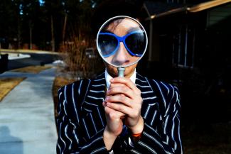 person using magnifying glass enlarging the appearance of his nose and sunglasses by Marten Newhall courtesy of Unsplash.