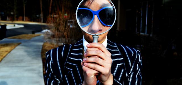 person using magnifying glass enlarging the appearance of his nose and sunglasses by Marten Newhall courtesy of Unsplash.